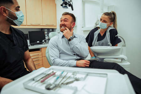 Caucasian male patient sitting in doctors chair explaining painful toothache to male and female nursesの写真素材