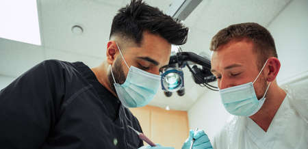 Two male dentists wearing surgical masks operating on patientの写真素材