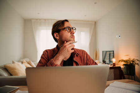 Caucasian male working from home typing on laptop thinking into space