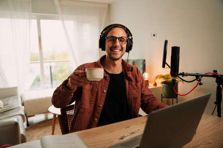 Caucasian male popular free lance podcaster drinking coffee and smiling while enjoying live conversationの写真素材
