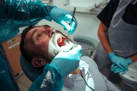 Caucasian male sitting with mouth wide open while male dentist cleans teethの写真素材