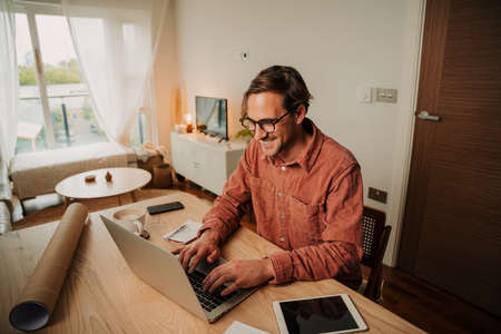 Caucasian male student typing on laptop working at home desk set up