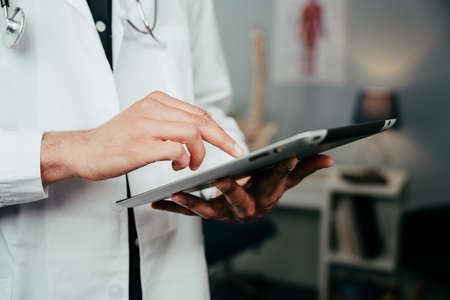 Male nurse standing in clinic typing on digital tabletの写真素材