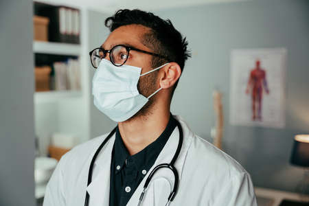 Mixed race male doctor working in clinic wearing surgical maskの写真素材