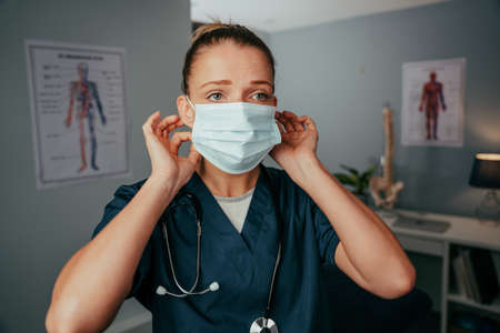 Caucasian female nurse wearing surgical mask standing in doctors clinic