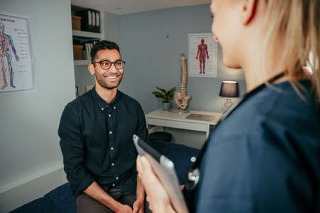 Mixed race male patient chatting to female nurse standing in clinic