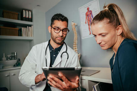 mixed race female nurse sitting with male doctor using digital tablet