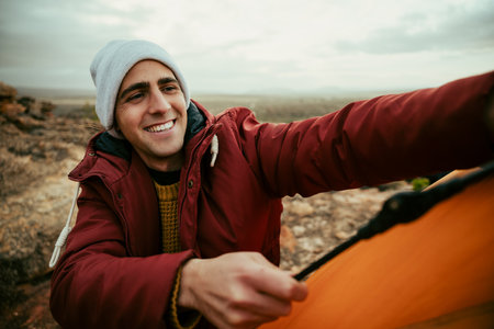 Caucasian male hiker pitching tent on top of mountain camping with friendsの写真素材