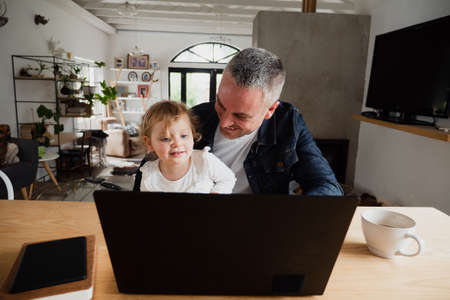Father and daughter watching family videos on laptop drinking coffee.