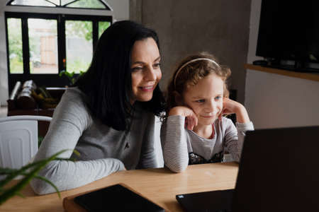 Happy mother and kid daughter looking at laptop, smiling mom and child girl having fun with online video on computerの写真素材