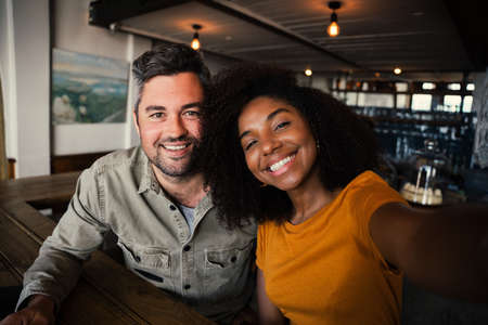 multi race couple smiling happily into camera in bright coffee shop
