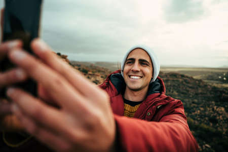 Caucasian male hiker taking selfie reaching top of mountain with big smileの写真素材