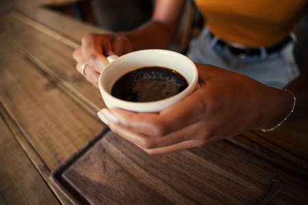 Aesthetic woman gently holding warm cup of coffee while sitting in trendy cafe.の写真素材