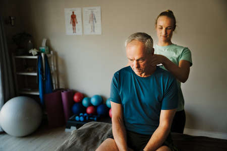 Woman therapist treating neck and back of elderly patient, diagnosis and recoveryの写真素材