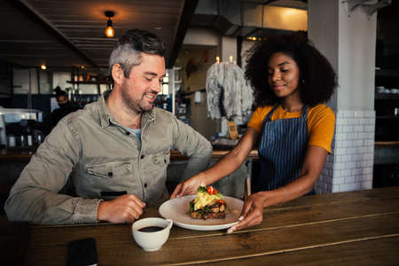 Ethnic waitress serving customer fresh egg breakfast at funky coffee shopの写真素材