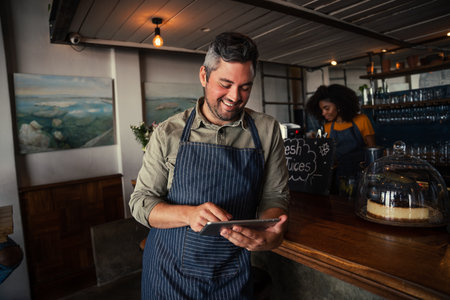 handsome and smiling male coffee shop owner browsing on tablet in coffee shop .の写真素材