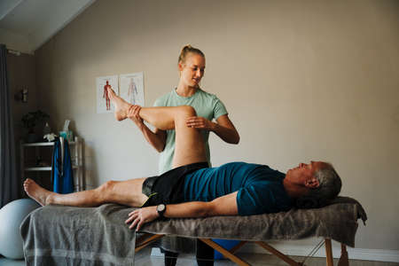 female physiotherapist performs knee assessment for elderly man