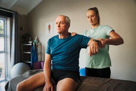 Therapist examining elderly patients shoulder in consultation room or rehabilitation clinicの写真素材