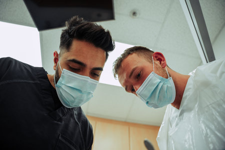 Two caucasian male doctors wearing surgical gear looking down on patientの写真素材