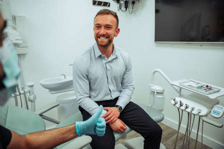 Caucasian male patient sitting in doctors chair smiling while dentist give him a thumbs up
