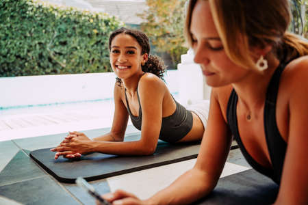 Two friends relaxing outside working out from home typing on cellular deviceの写真素材