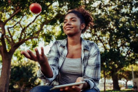 Mixed race female holding digital tablet researching project on healthy foods while playing with fresh red tomatoの写真素材