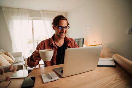 Caucasian male student on video call with classmates working from home drinking coffeeの写真素材