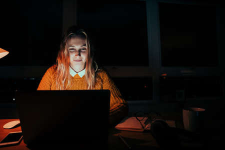 Caucasian female student working late at night typing on laptop working from home officeの写真素材