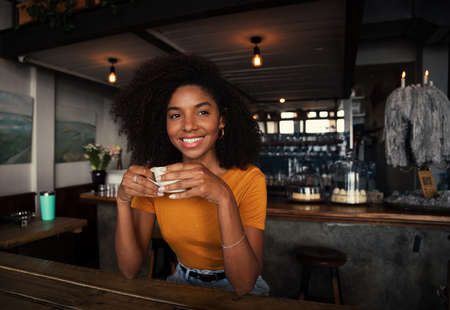 Beautiful female smiling looking in the distance enjoying hot coffee in trendy cafeの写真素材