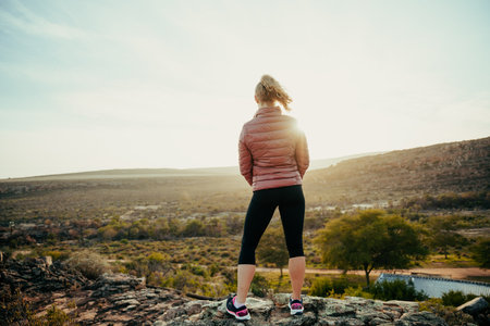 Caucasian female hiking standing on mountain top admiring sunset