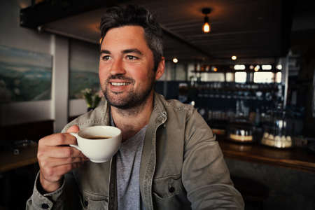 Handsome male customer drinking hot coffee in trendy cafeの写真素材