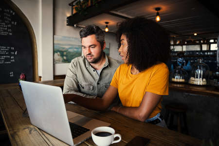 Cute couple deciding on decor for new house searching on laptop sitting at funky restaurantの写真素材
