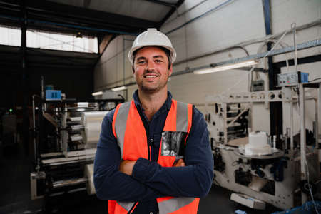 Male engineer standing smiling with crossed arms in factoryの写真素材