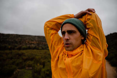 Concentrating young male athlete stretching shoulder with elbow before long distance run up mountain trail in cloudy weatherの写真素材