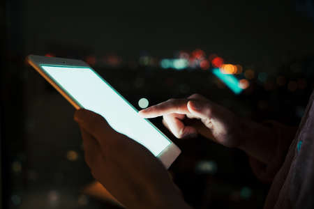 Close up of male business man working on digital tablet working late at night in apartment officeの写真素材