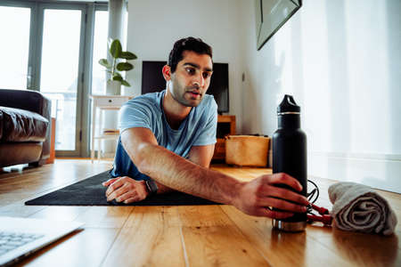 Mixed race male working out in living room reaching for bottle feeling tiredの写真素材