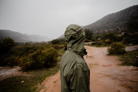Young fit male runner resting from running on gravel mountain path in rain with rain jacket cloudy weather green bushesの写真素材