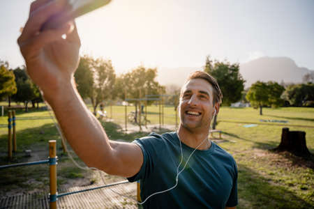 Young male athlete taking picture of self with smartphone listening to music with ear phones in...