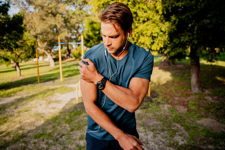 Injured young male athlete looking concerned holding shoulder in pain after exercising outdoors with...