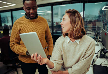 Caucasian female designer unimpressed with designs made by male partner looking on digital tablet...