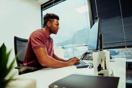African American male entrepreneur researching logo designs for company using desktop laptop sitting in fancy officeの写真素材