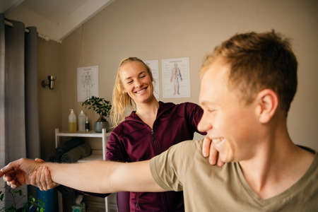 Female physiotherapist stretching arm of caucasian patient.