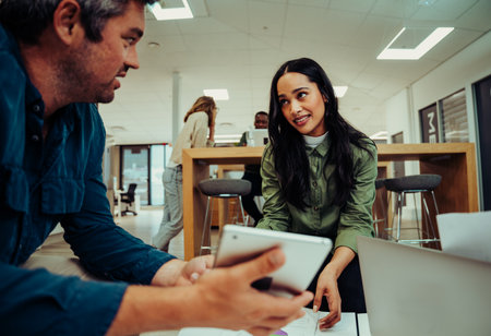 Mixed race female giving tips to business man to improve his project sitting in office loungeの写真素材