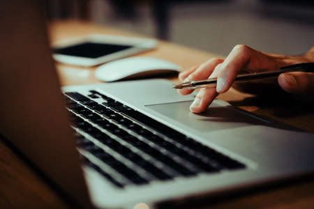 Close up of young caucasian male working on laptop scrolling through emails late at nightの写真素材