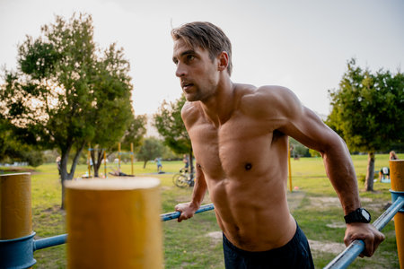 Strong attractive young male athlete shirtless focused on exercising arms for strength on bars using...