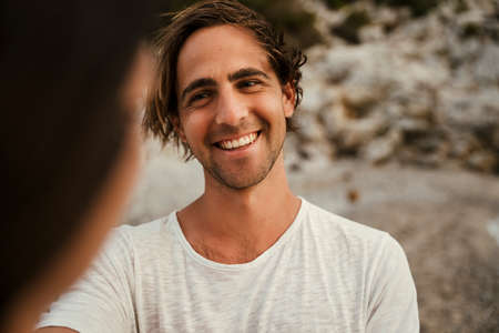 Caucasian male smiling while staring at girlfriend while standing on the beachの写真素材