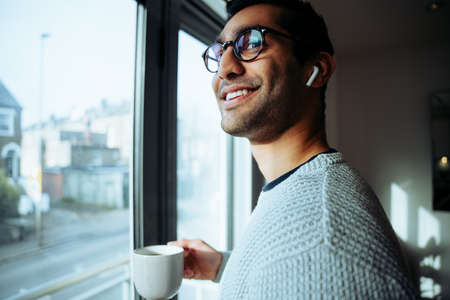 Smiling mixed race business man working from home enjoying hot morning coffee listening to music...