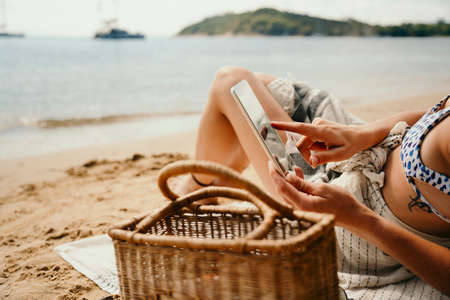 Caucasian female relaxing on beach reading book off digital tablet