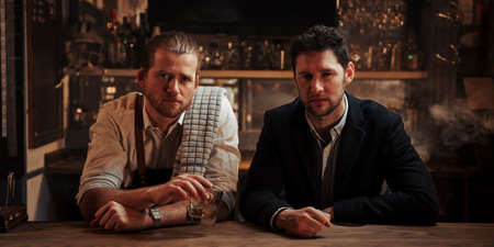 Caucasian bartender and manager sitting at bar drinking from whiskey glass