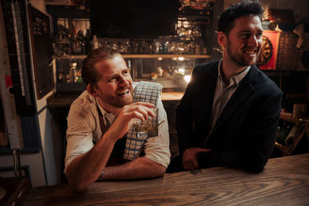 Caucasian male bartender having a drink with male manager at the bar
